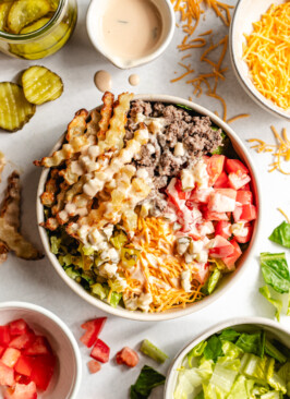 A venison burger bowl topped with sauce with fresh ingredients surrounding it