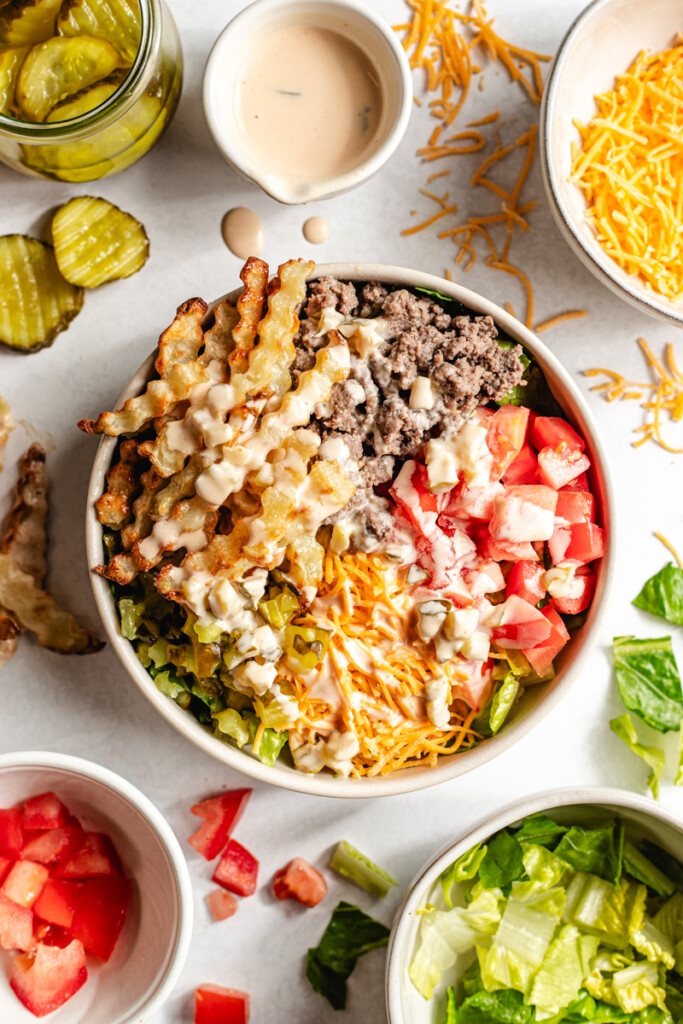 A venison burger bowl topped with sauce with fresh ingredients surrounding it