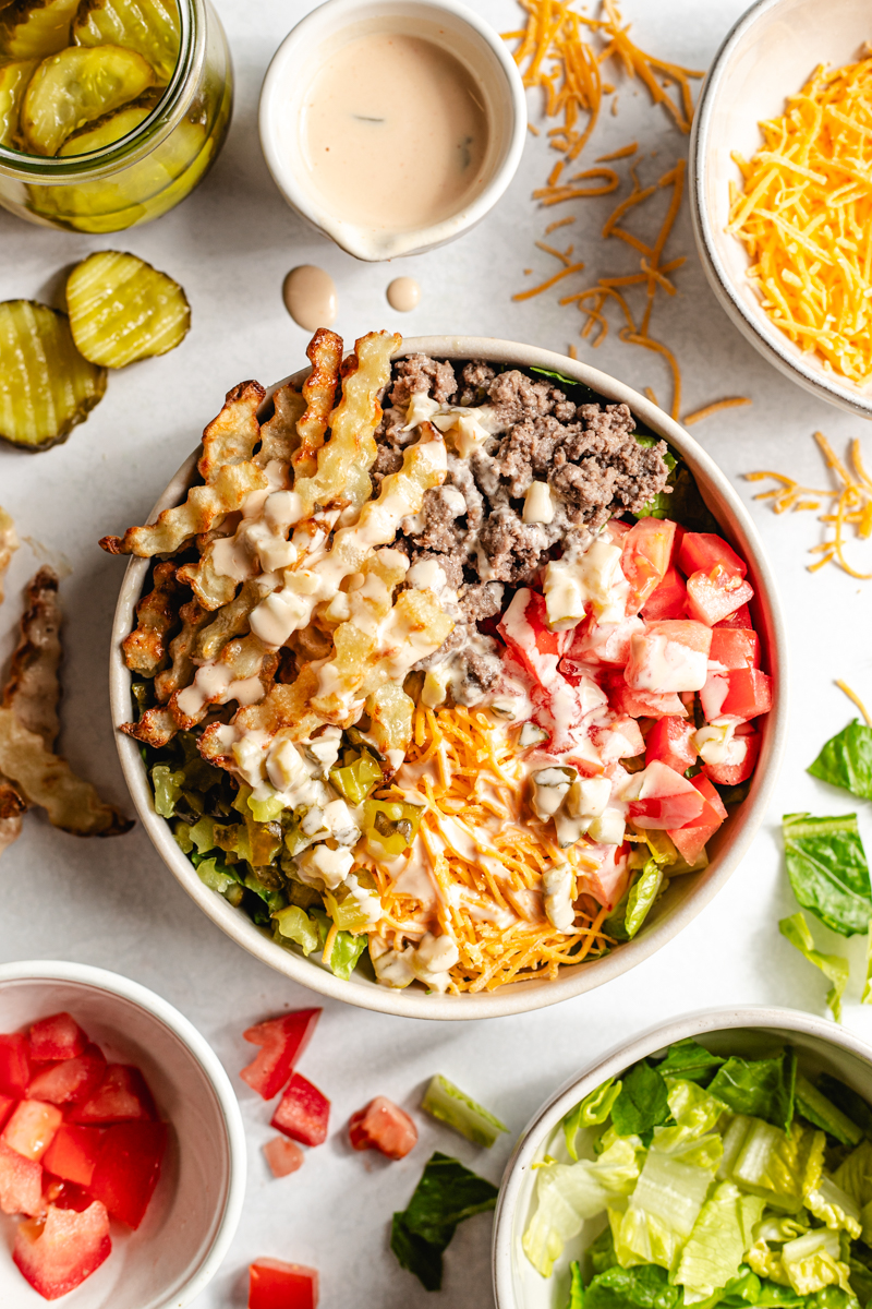 A venison burger bowl topped with sauce with fresh ingredients surrounding it