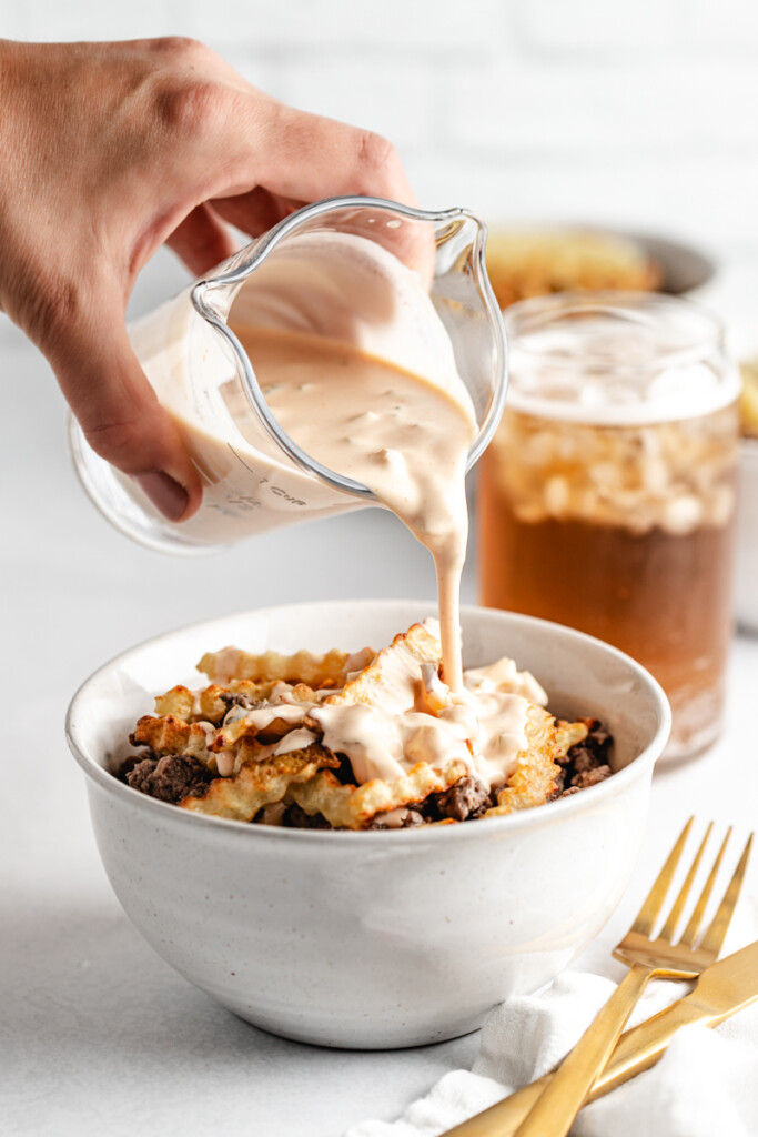 Sauce being poured over a prepared venison burger bowl
