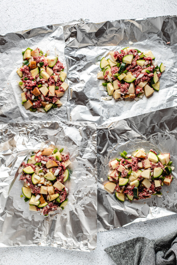 Four pieces of tin foil with venison, potatoes, vegetables and seasoning mixed on each