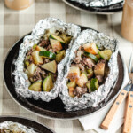 Venison foil packs opened on black camping plates with forks