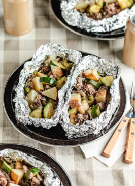 Venison foil packs opened on black camping plates with forks