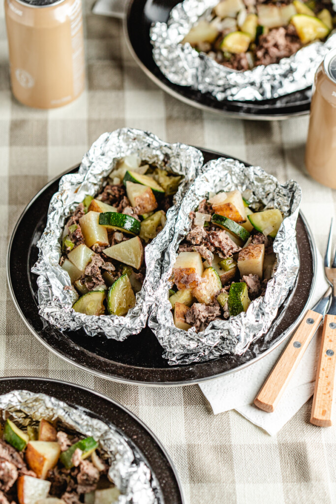 Venison foil packs opened on black camping plates with forks