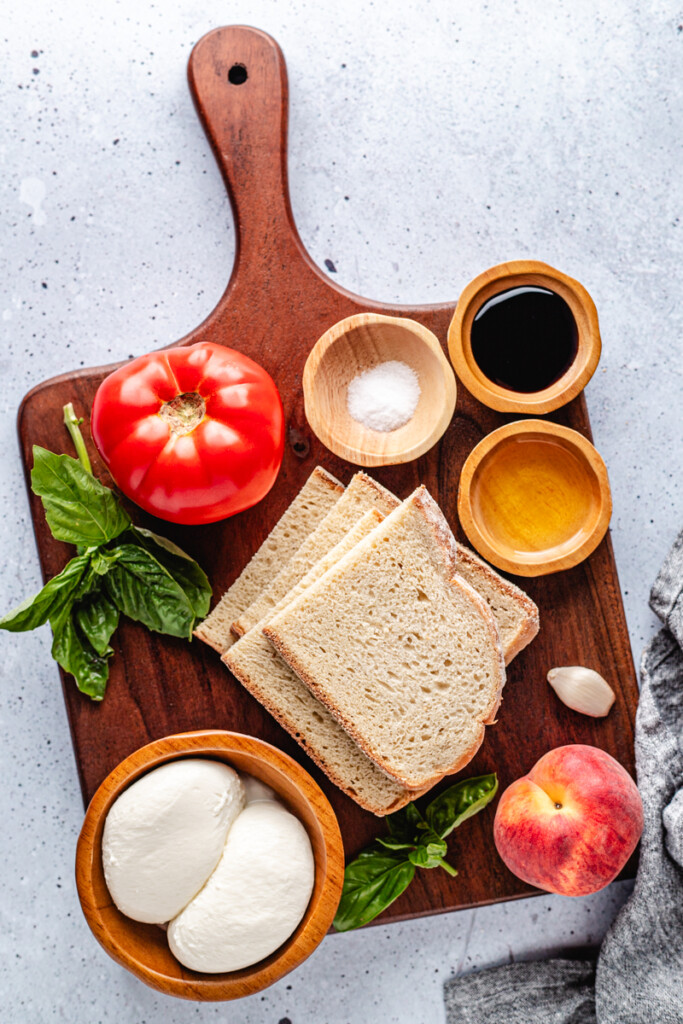 Ingredients to make Peach Burrata Toast on wooden cutting board