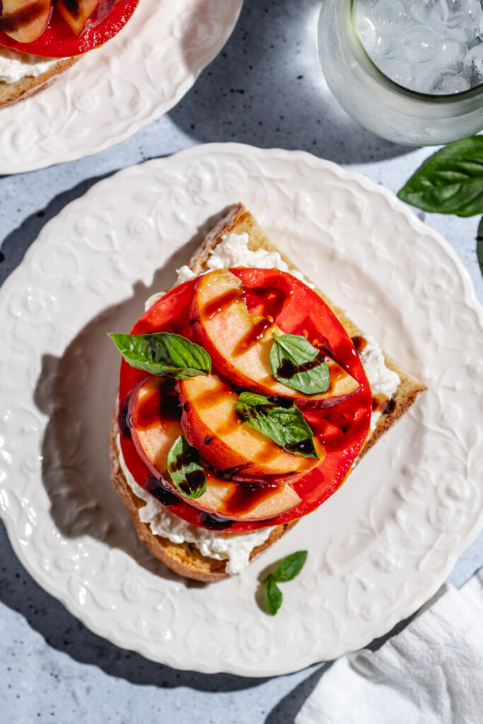 A piece of Peach Burrata Toast on a white plate
