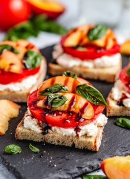 Peach Burrata Toast on a black slate with balsamic glaze dripping off the front piece
