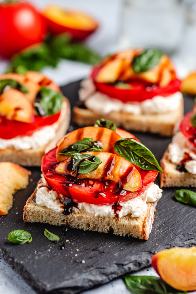 Peach Burrata Toast on a black slate with balsamic glaze dripping off the front piece