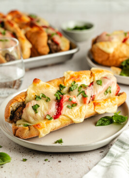 A meatball sub on a white plate garnished with basil