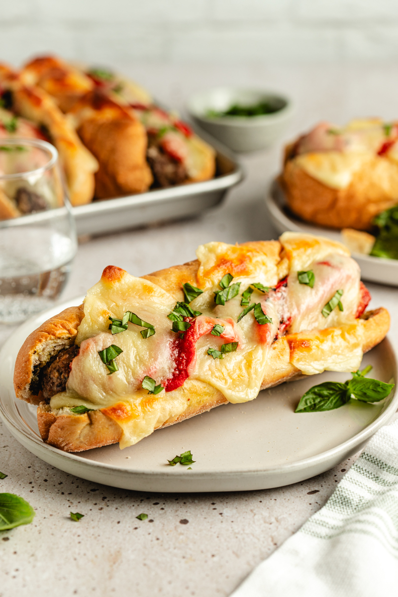 A meatball sub on a white plate garnished with basil