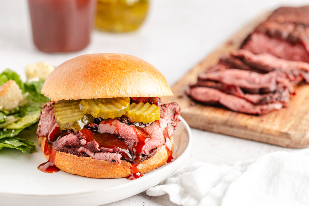 A sandwich with thinly sliced smoked venison, bbq sauce and pickles