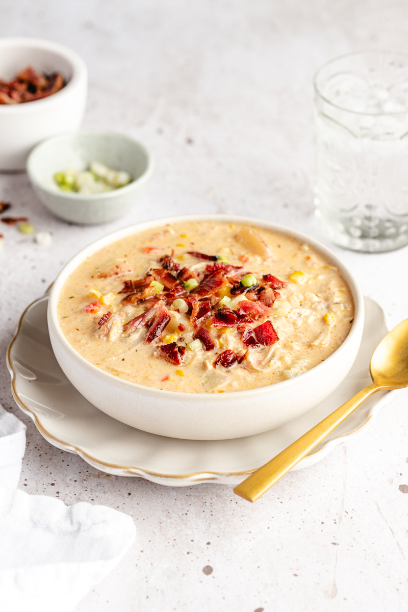 Chicken corn chowder in a white bowl garnished with bacon and green onions