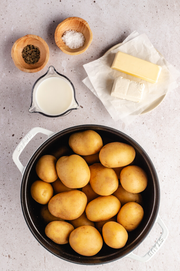 Ingredients to make mashed potatoes including gold potatoes, milk, butter, cream cheese, salt and pepper
