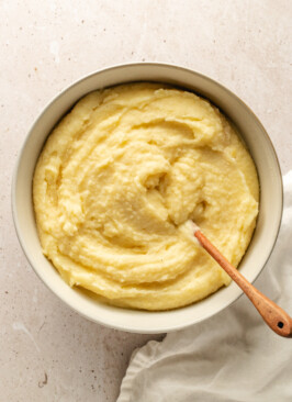 Mashed potatoes in a white bowl stirred with a wooden spoon