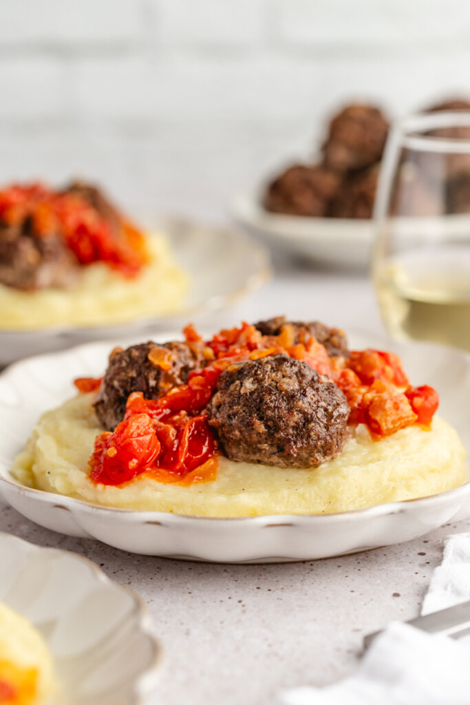 Stuffed meatballs served on a white plate with mashed potatoes and tomato bacon jam