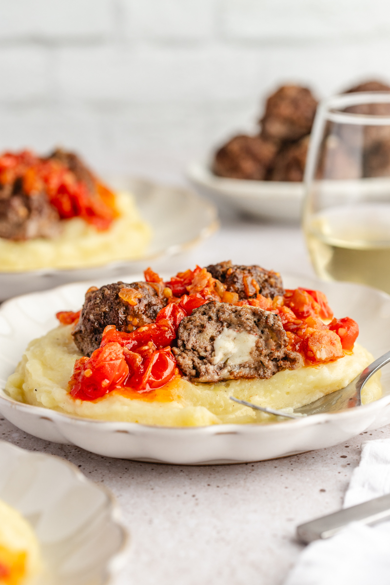 Pepper jack cheese inside of a cut in half meatball served with mashed potatoes and bacon jam