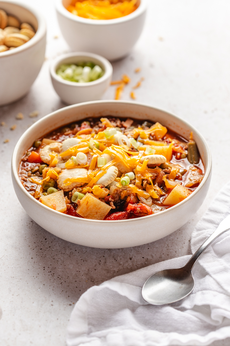 A bowl of hamburger soup in a white bowl served with toppings