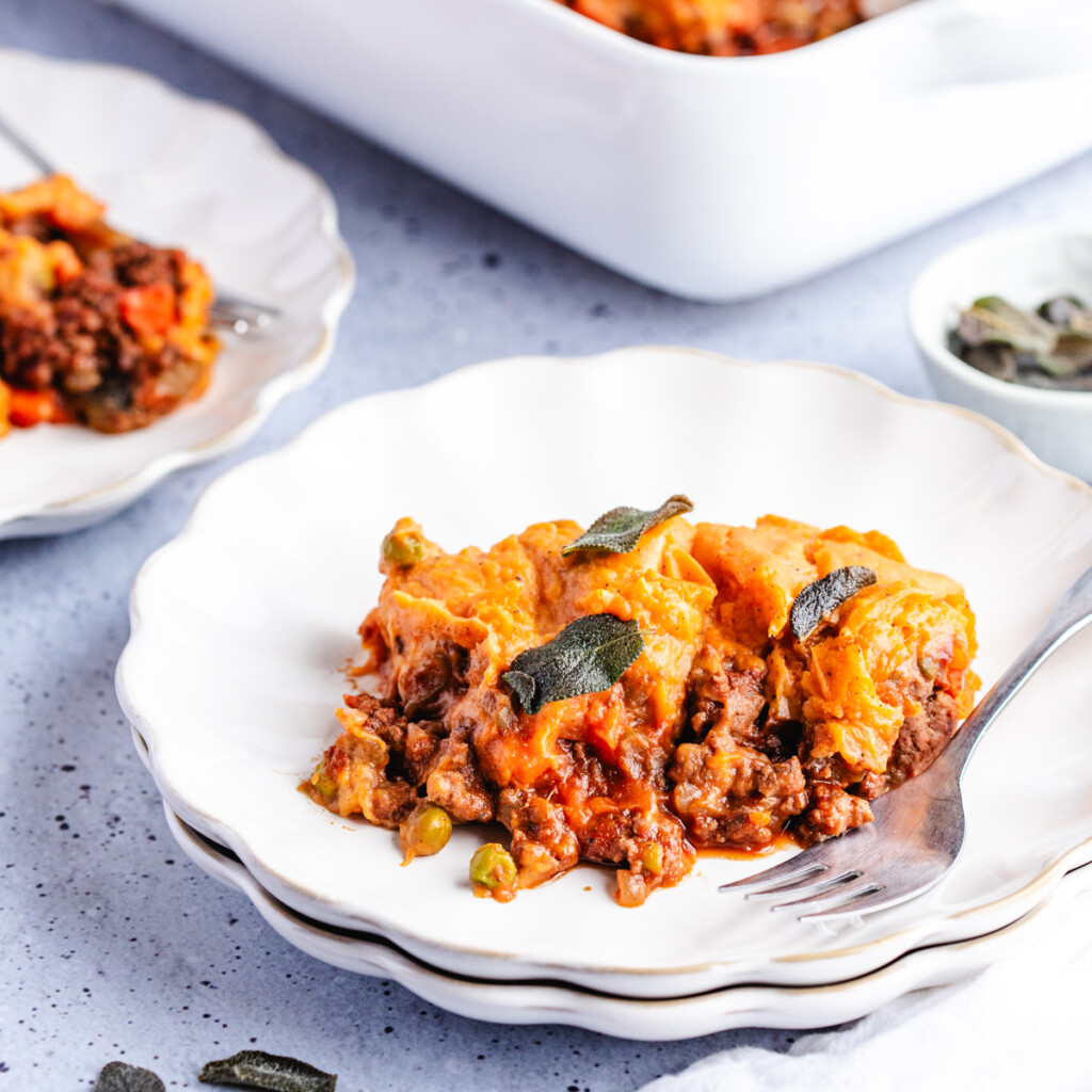 A serving of Sweet Potato Shepherd's Pie on a white plate garnished with crispy sage