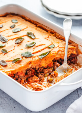 A white casserole dish of Sweet Potato Shepherd's Pie with a serving spoon in it