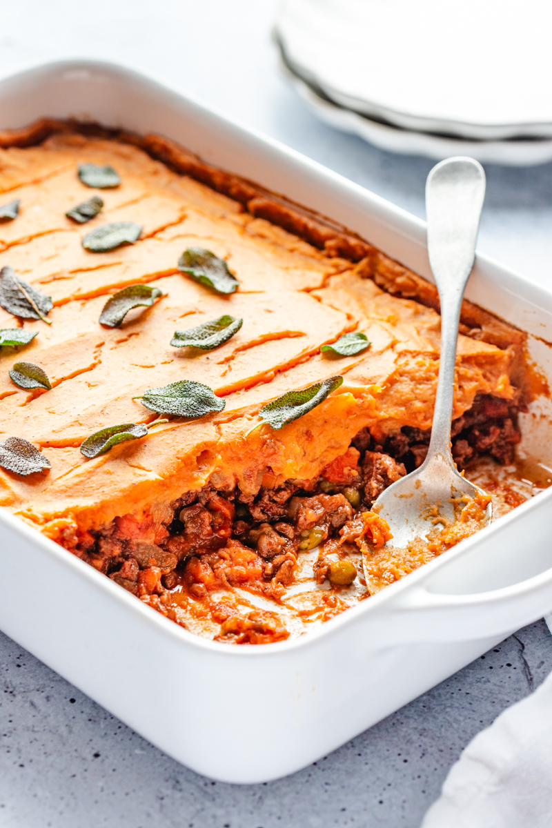 A white casserole dish of Sweet Potato Shepherd's Pie with a serving spoon in it