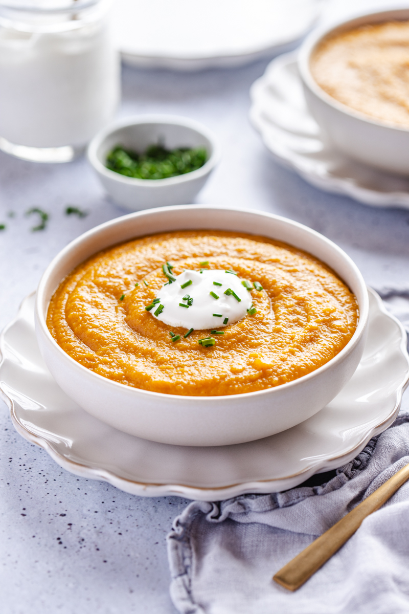 Butternut squash soup in a white bowl topped with sour cream and chives