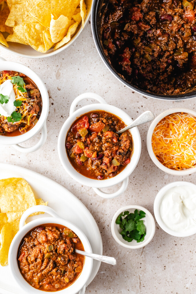 Pumpkin Chili served in white soup bowls with toppings of cheese, sour cream and cilantro