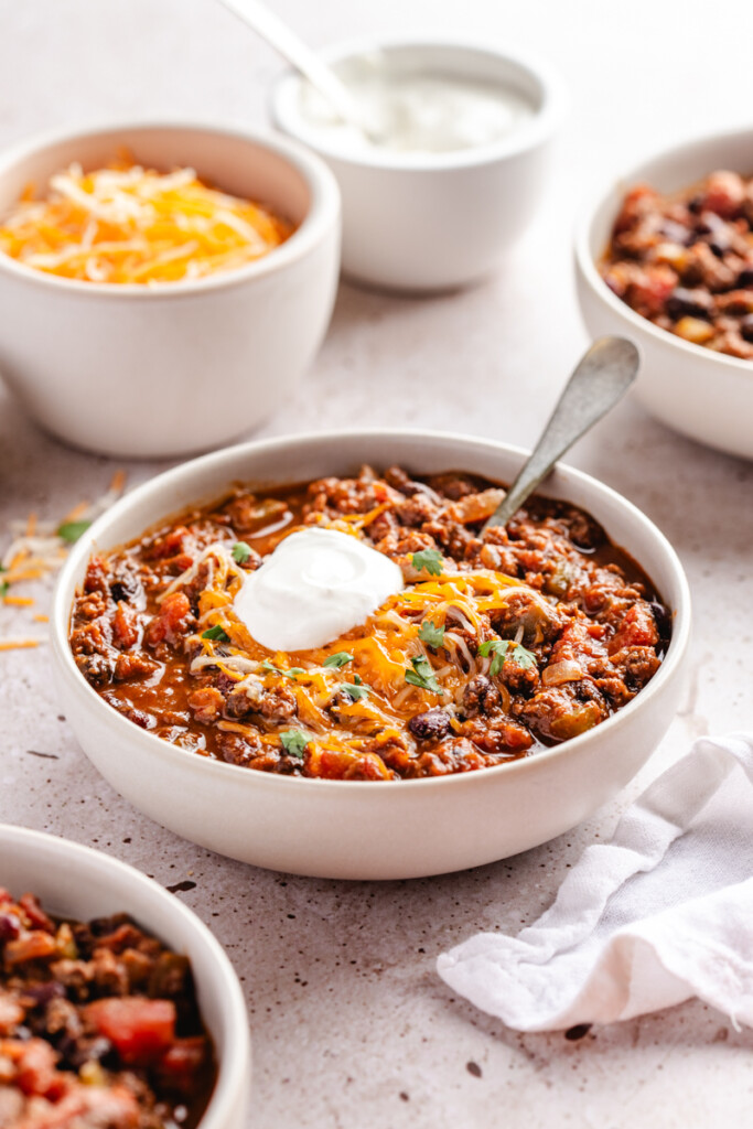 A white bowl with pumpkin chili topped with a dollop of sour cream, cilantro and shredded cheese