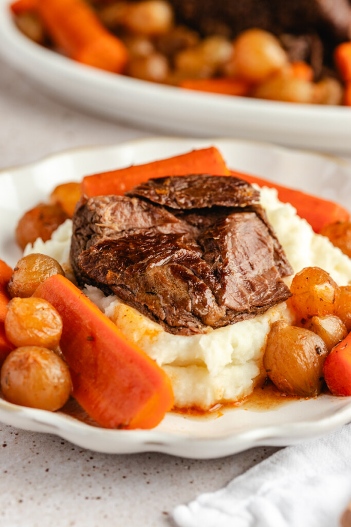 Venison roast served over potatoes, plated with carrots and pearl onions
