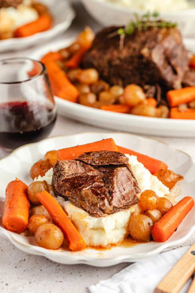Beer Braised venison roast served on a white plate with mashed potatoes, carrots and pearl onions