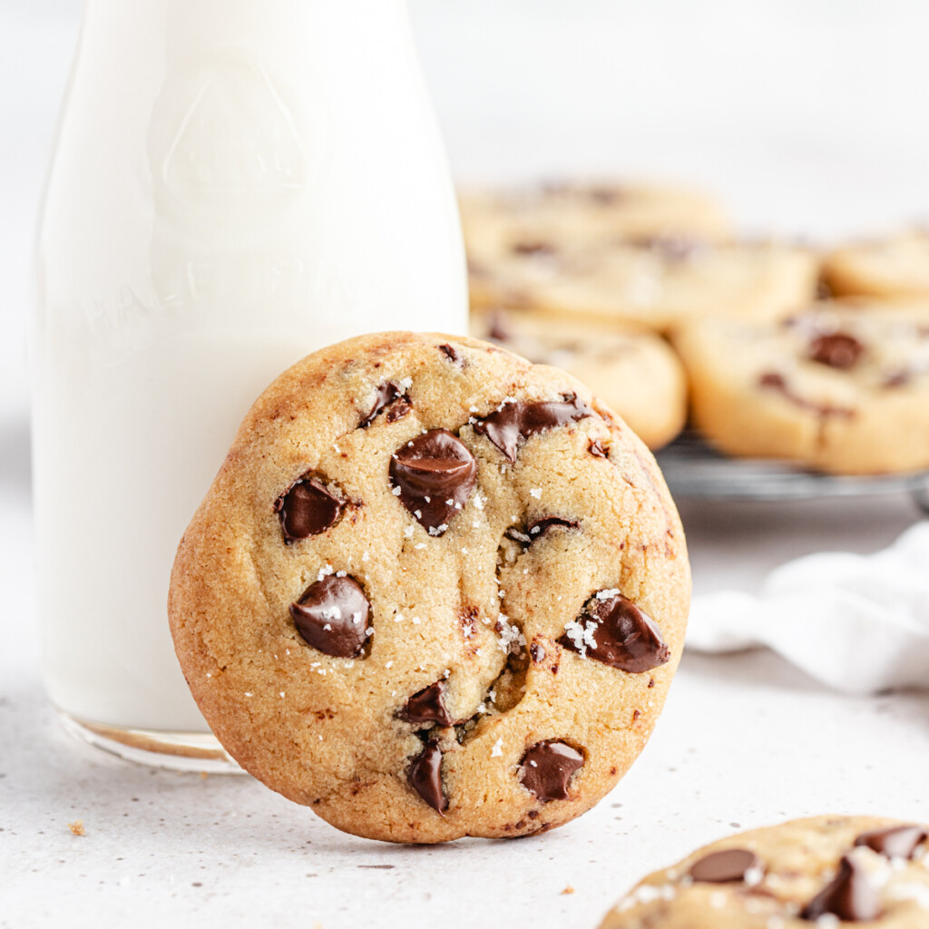 A close up of a Brown Butter Chocolate Chip Cookie leaning on a glass of milk