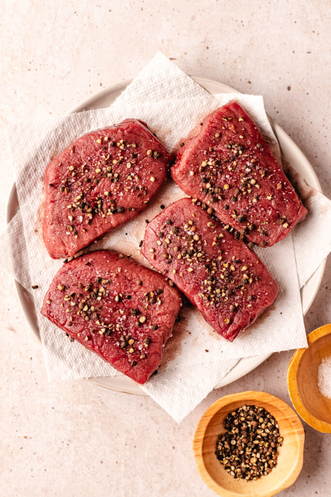 4 venison steaks coated with salt and crushed peppercorns on a paper towel lined plate