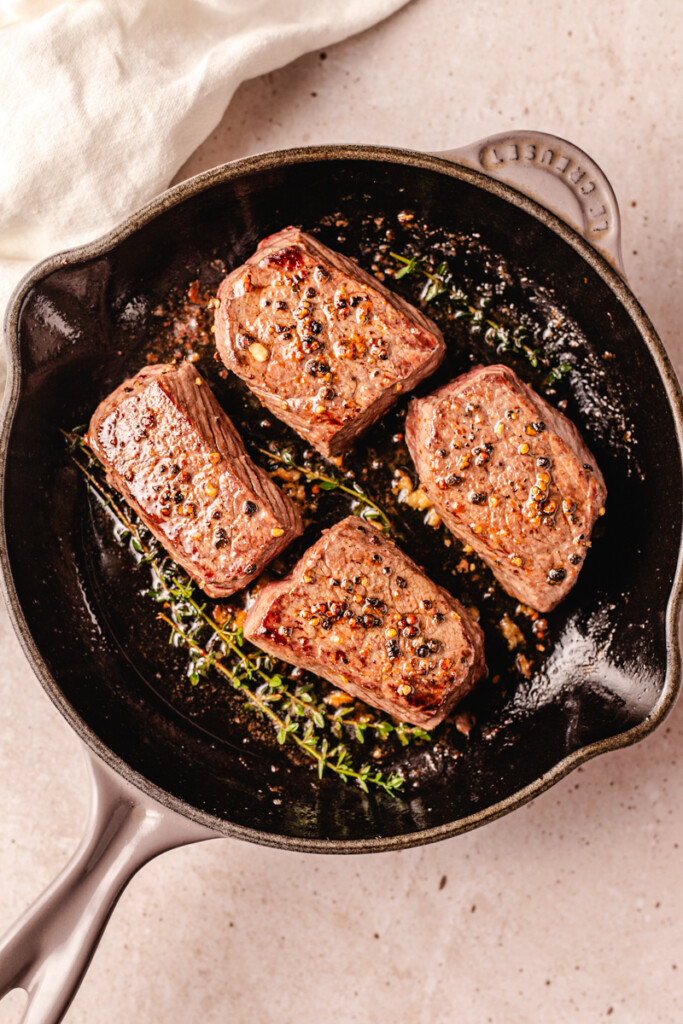 4 venison steaks in black skillet basted with butter, garlic and thyme sprigs