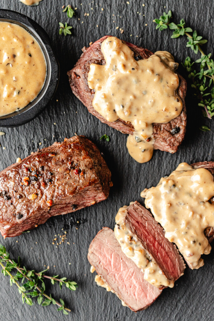 Venison Au Poivre on a black slate with sauce and thyme sprigs