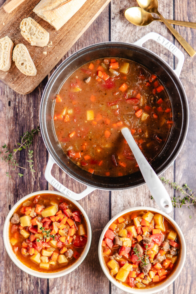 Venison stew in soup pot with two white bowls filled with soup