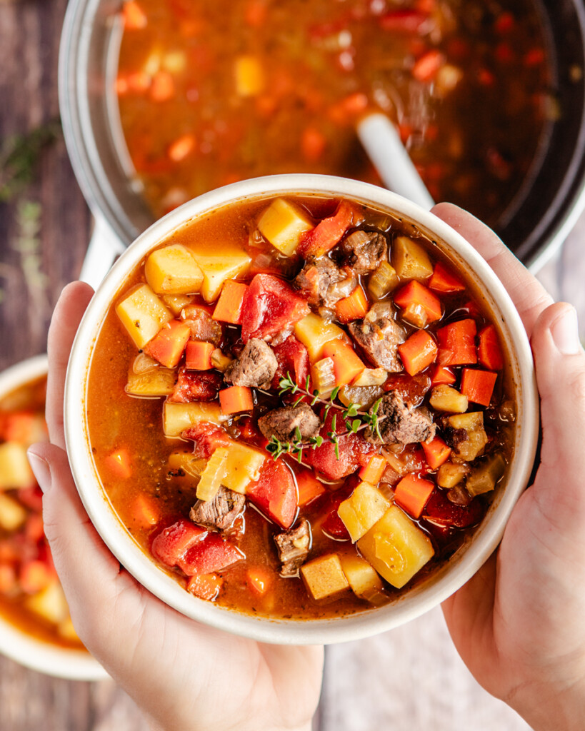 Two hands holding stew in a white bowl