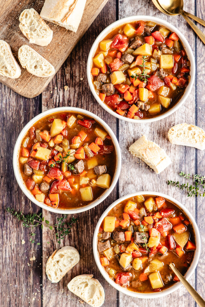 Three white bowls of venison stew with crusty bread surrounding it
