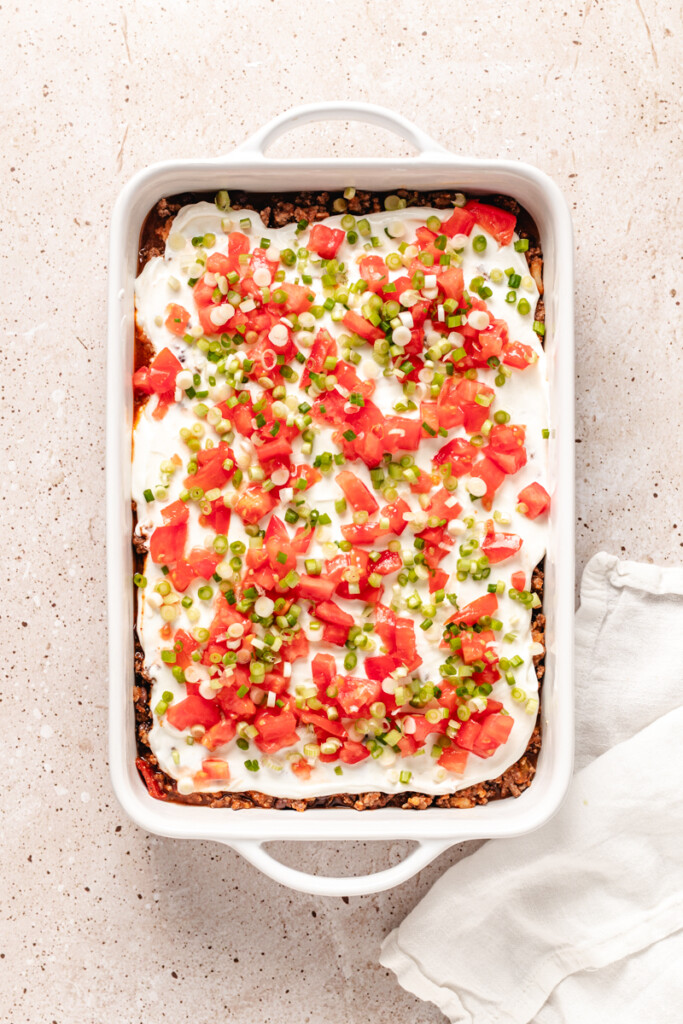 taco casserole topped with greek yogurt, dices tomatoes and green onions.
