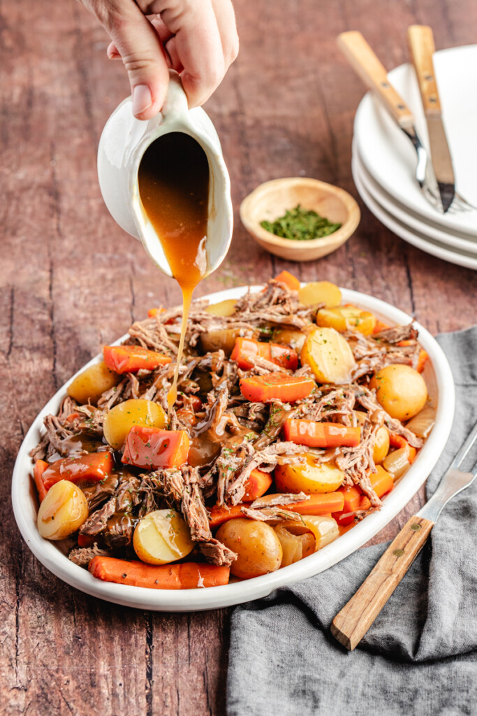 Gravy being poured over meat and potatoes