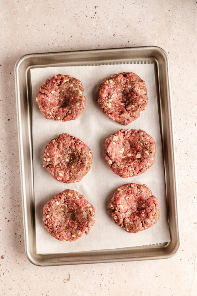 Six venison slider patties on a tray with indents in the middle