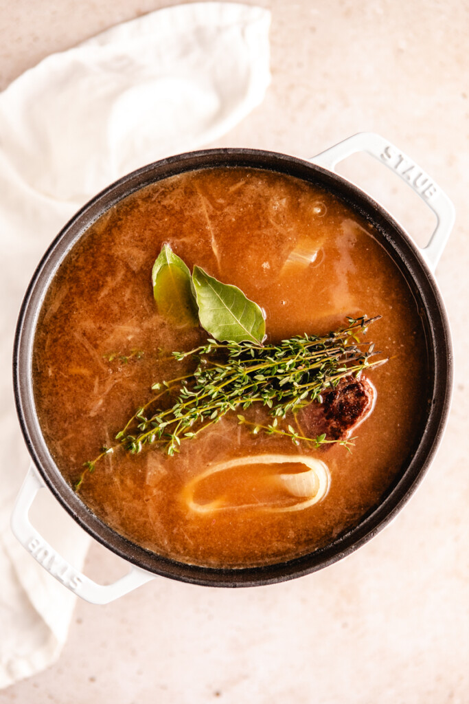Onions, broth and roast simmering in a dutch oven with bay leaves and thyme