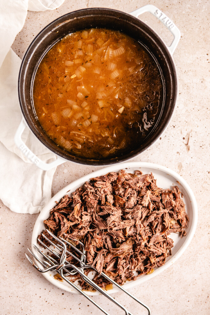 French onion soup in a dutch oven and shredded braised meat on a white platter