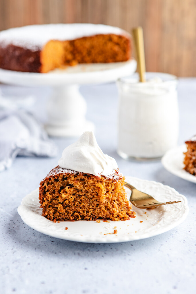 A slice of Fresh Ginger Orange cake with a bite taken out of it on a white plate with a gold fork