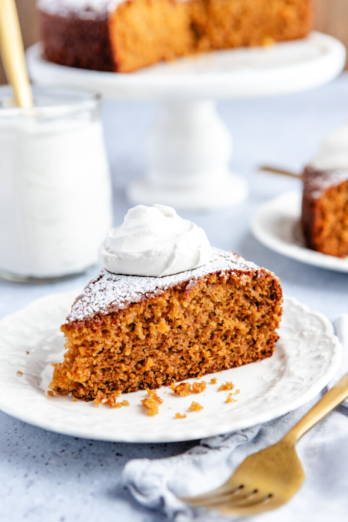 A piece of Fresh Ginger Orange cake on a white plate topped with thyme ginger cream