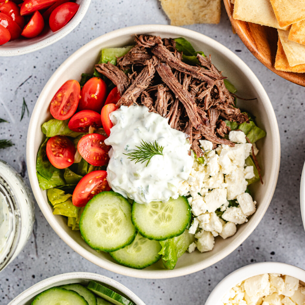 A Greek Venison Power bowl filled with lettuce, cherry tomatoes, cucumbers, shredded venison, feta cheese and tzatziki sauce