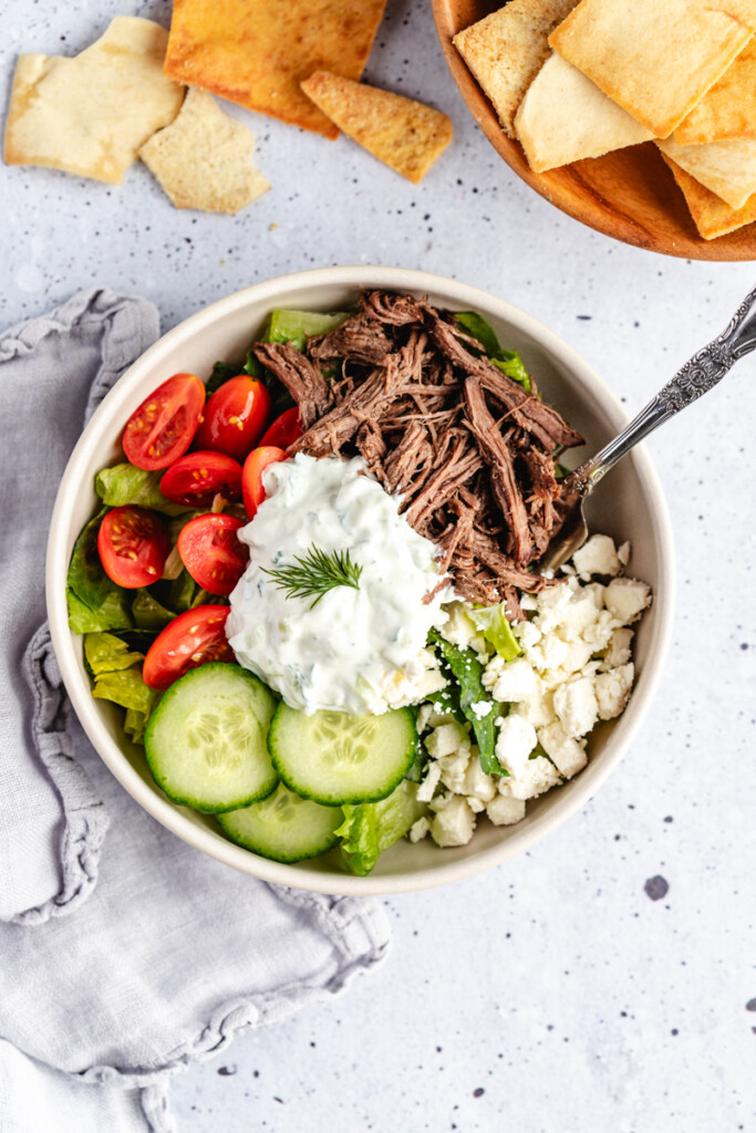 A fork digging into a Greek Venison power bowl with pita chips around it