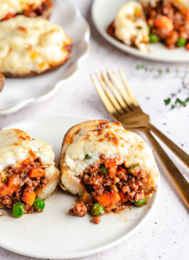 A Shepherd's Pie Stuffed Potato cut in half on a white plate with gold forks beside it