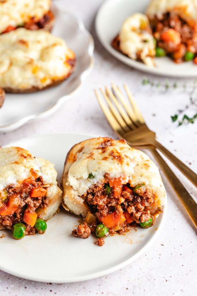 A Shepherd's Pie Stuffed Potato cut in half on a white plate with gold forks beside it