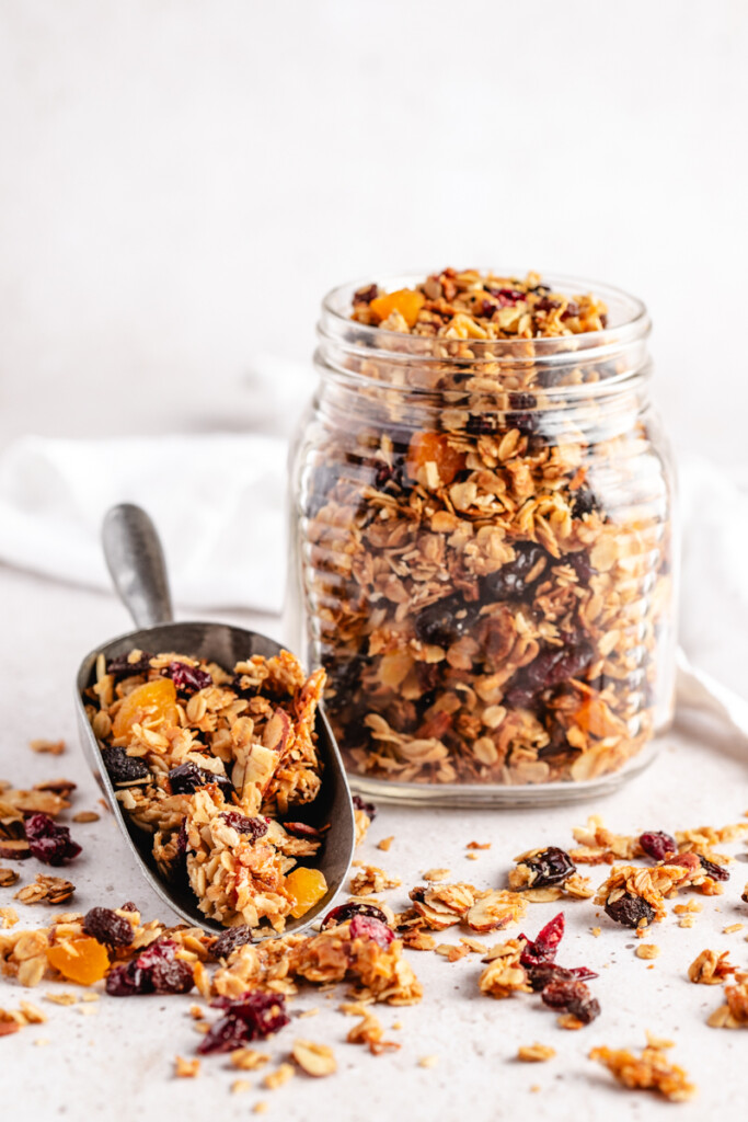 A scoop of granola in front of a glass jar filled with granola