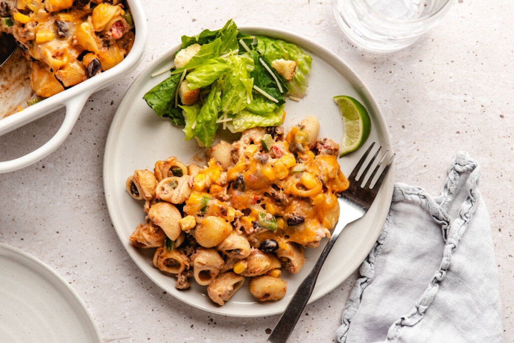 a piece of cheesy pasta bake in a white casserole dish with salad